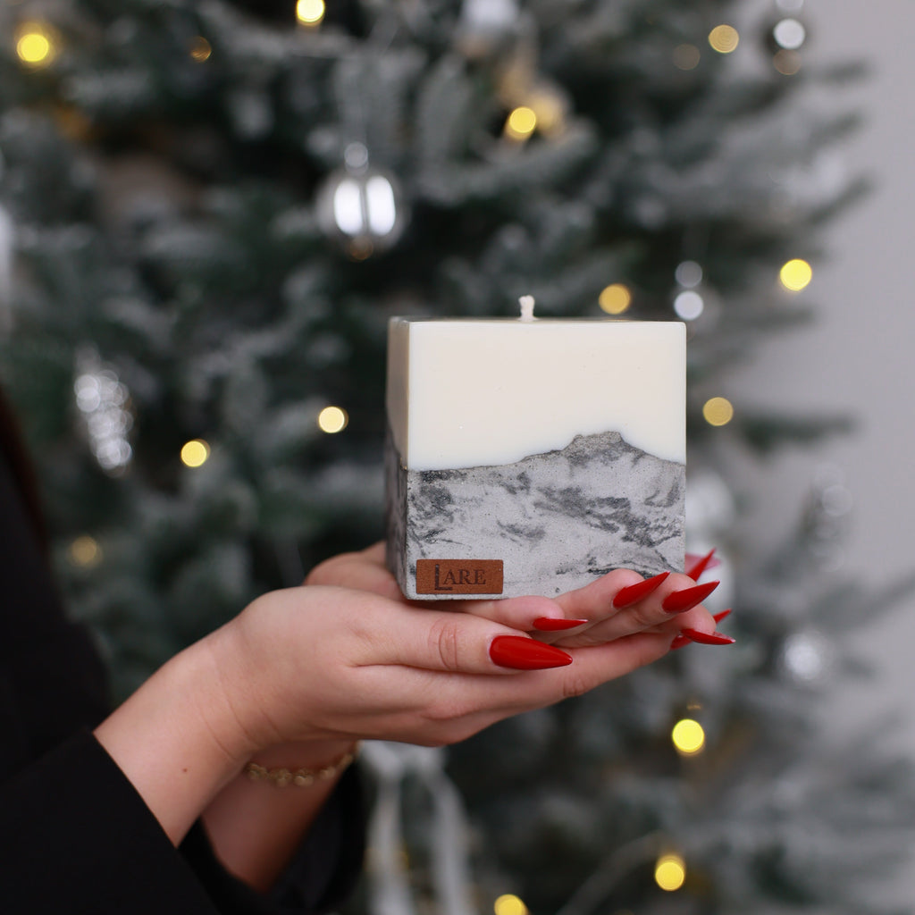Christmas candle by LARE — hand holding sculptural soy wax pillar with gray marble concrete base and signature LARE label