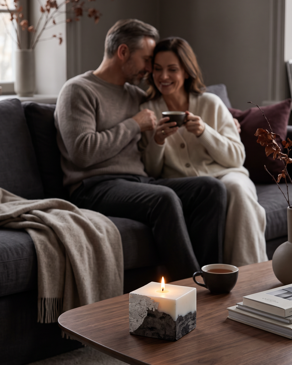 LARE best scented candle on a wooden coffee table as a couple relaxes on a dark sofa — sculptural candles for cozy living room interiors.