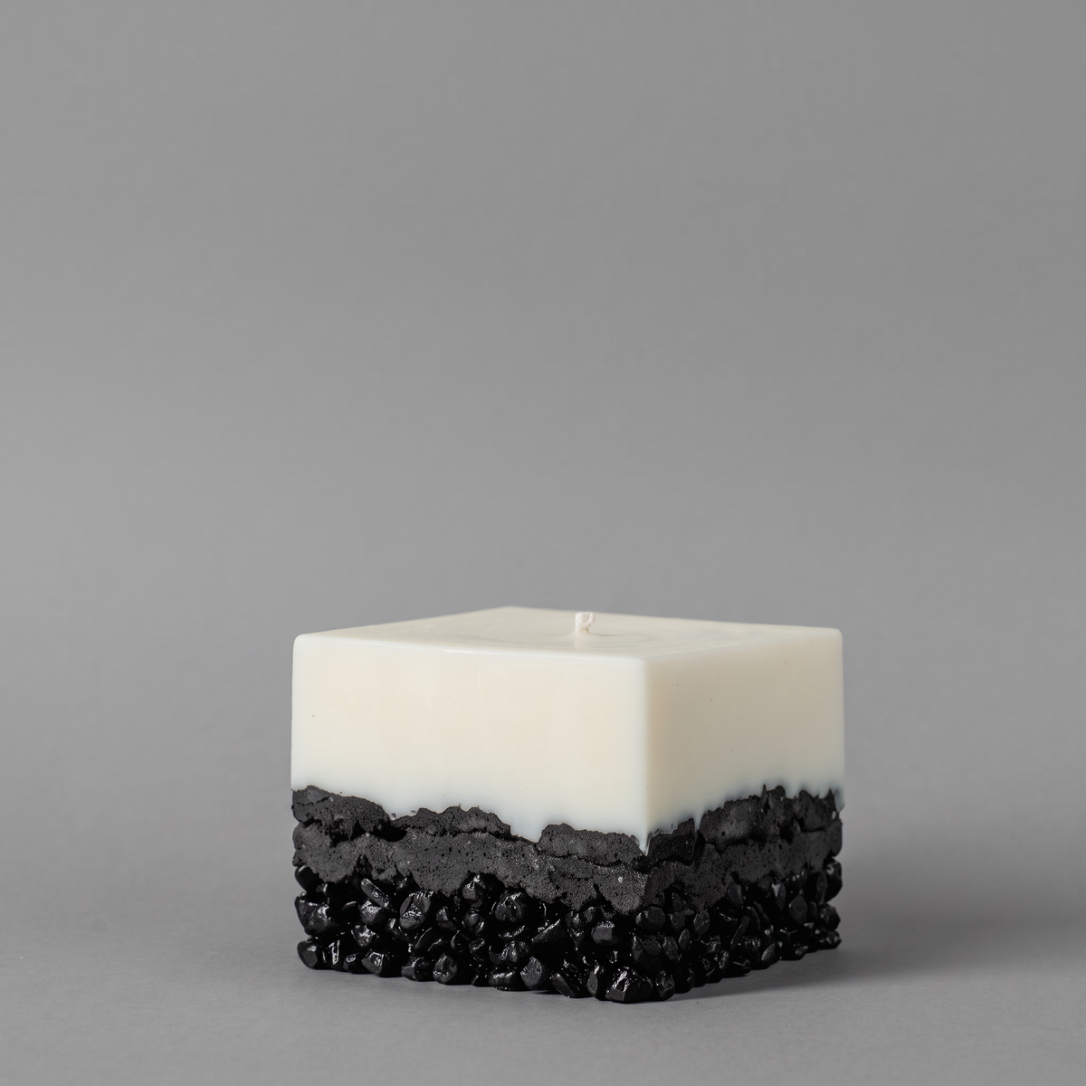A square layered candle with a smooth matte white top half and a textured black bottom half, serving as modern bathroom decor ideas on a plain gray studio background.