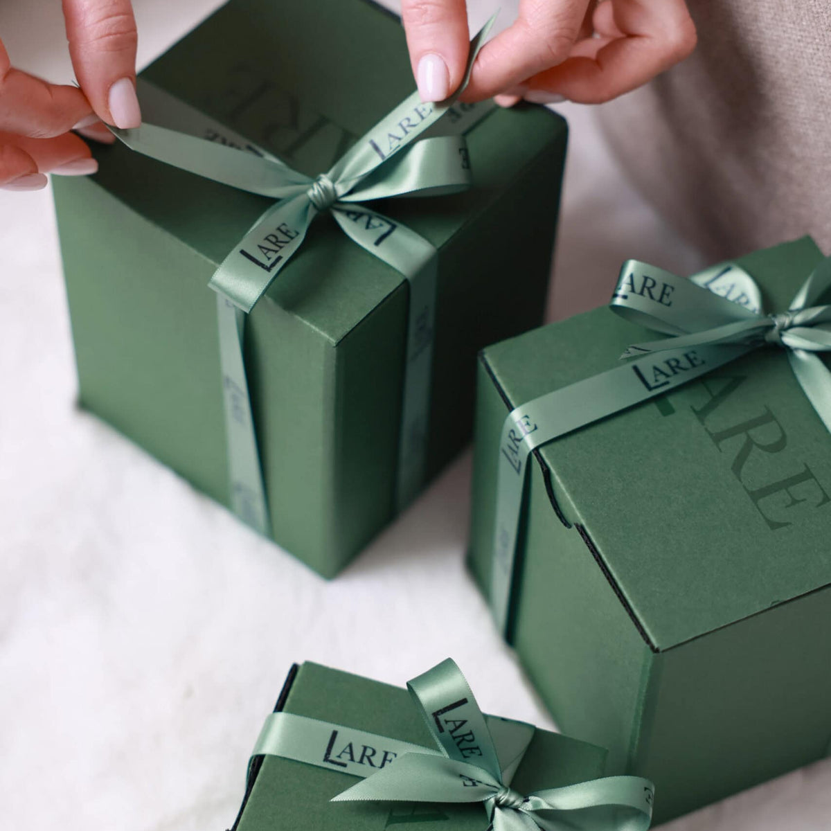 LARE Studio luxury gift photography featuring three elegant gift boxes with silk ribbons on a cozy light beige background, perfect for premium gift ideas.